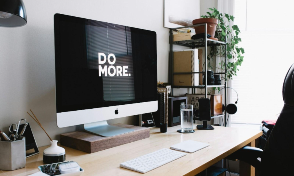 A desk with a computer monitor displaying a screen and a sign that says "Do More".