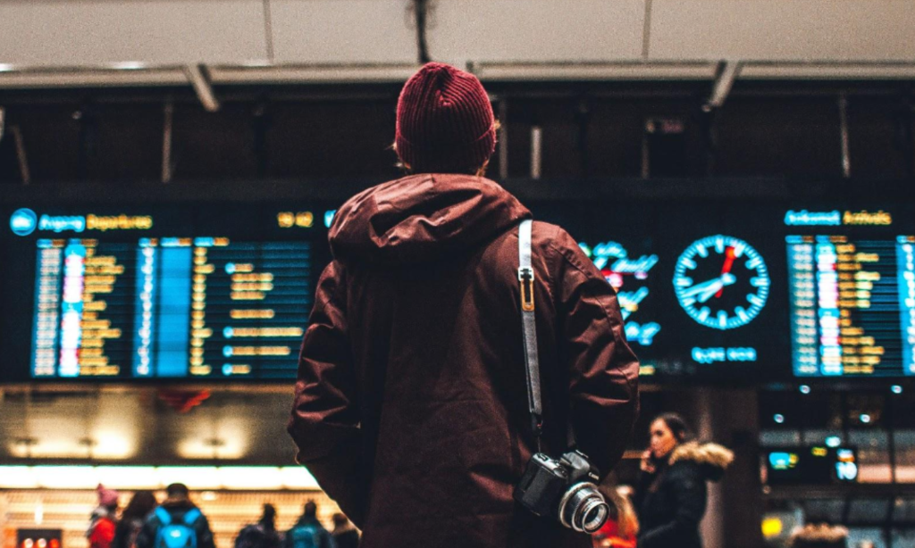 A man in a red jacket is standing in an airport with his camera