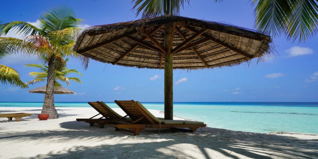 Two lounge chairs under an umbrella on a beautiful beach.