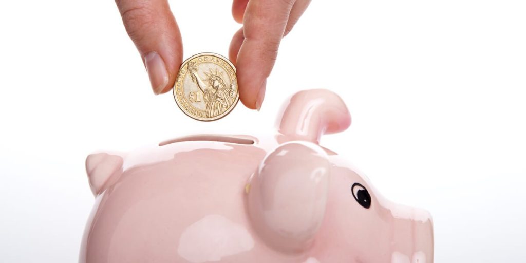 A person putting a coin into a pink piggy bank