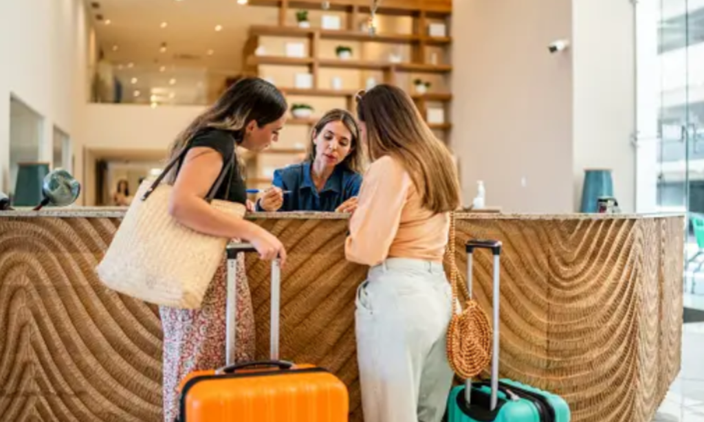 2. Two women checking in with luggage at hotel.