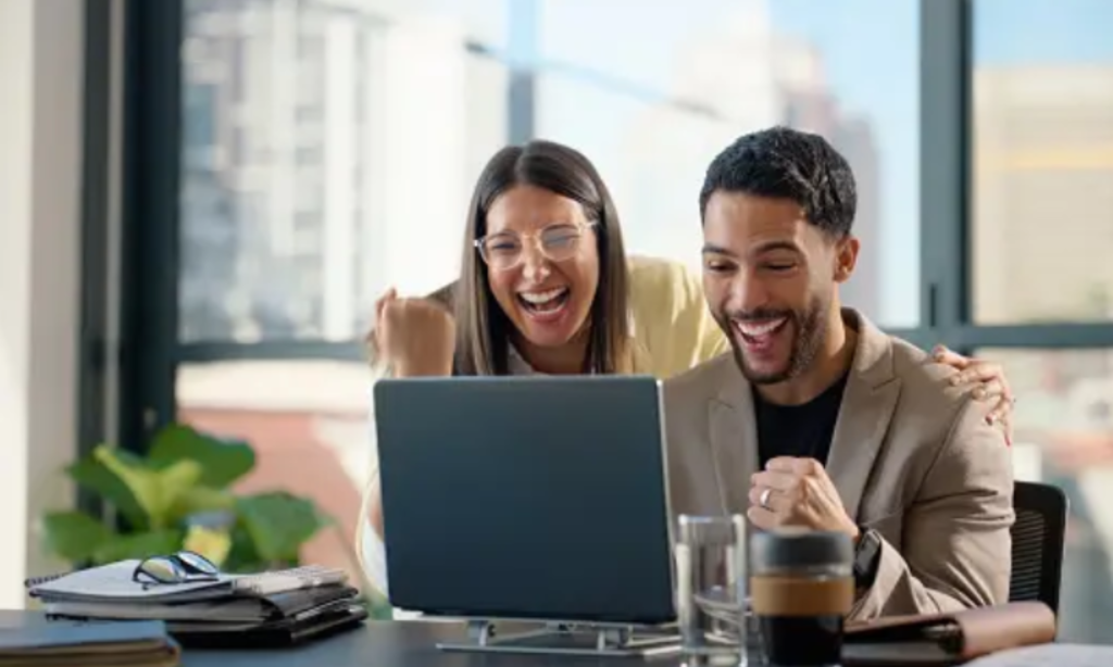 Two individuals joyfully laughing and smiling together while engaged with a laptop