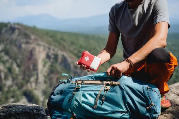 traveler on top of a cliff extracting a first aid kit from his bag pack